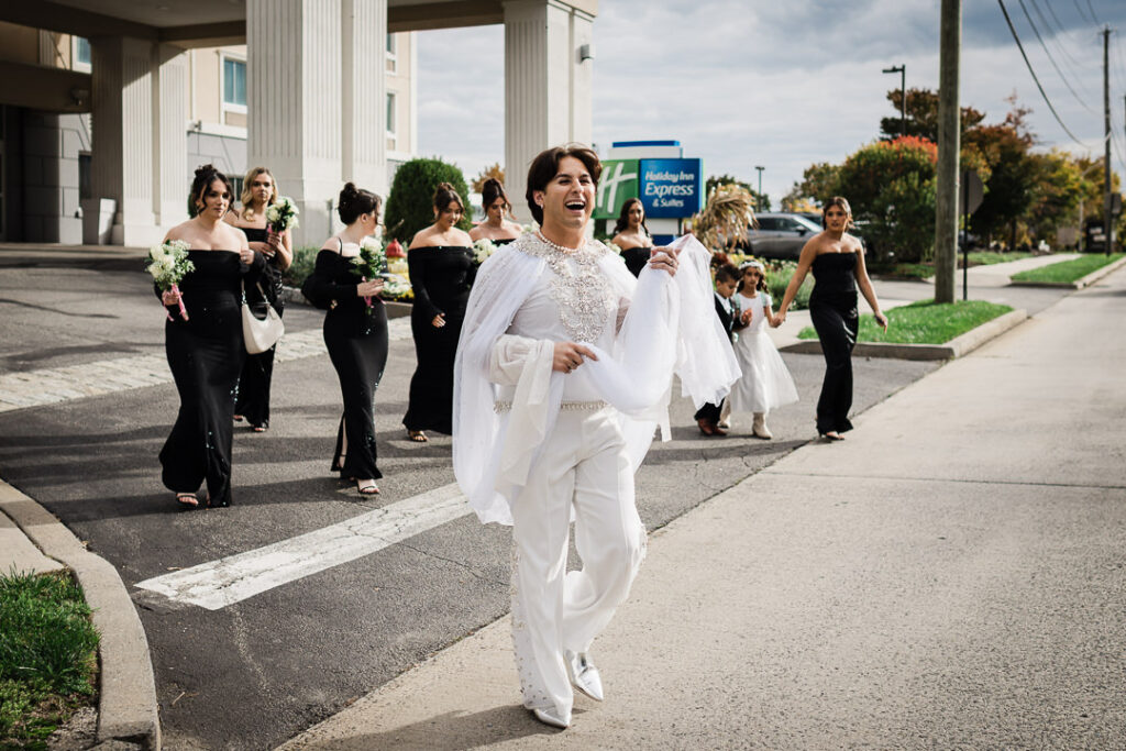 Bride in white beaded outfit with bridal party in black off-shoulder gowns walking on Peekskill street for fall Hudson Valley wedding