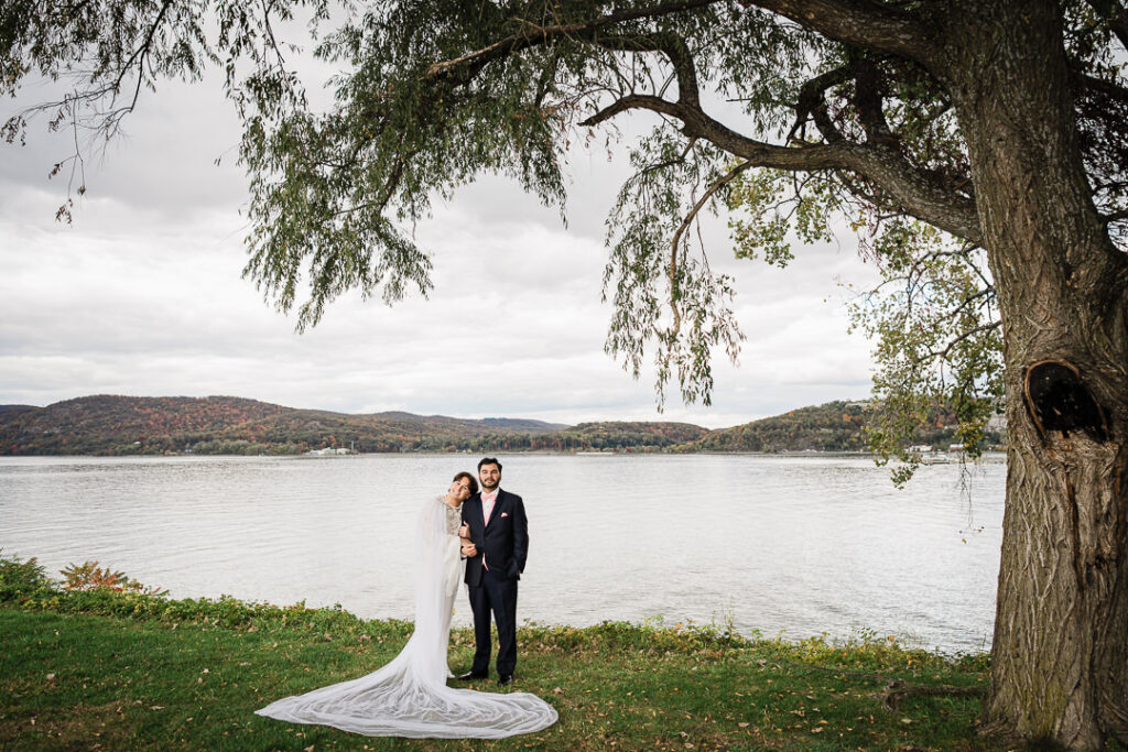 Couple jumping in celebration by Hudson River, joyful Peekskill wedding photo