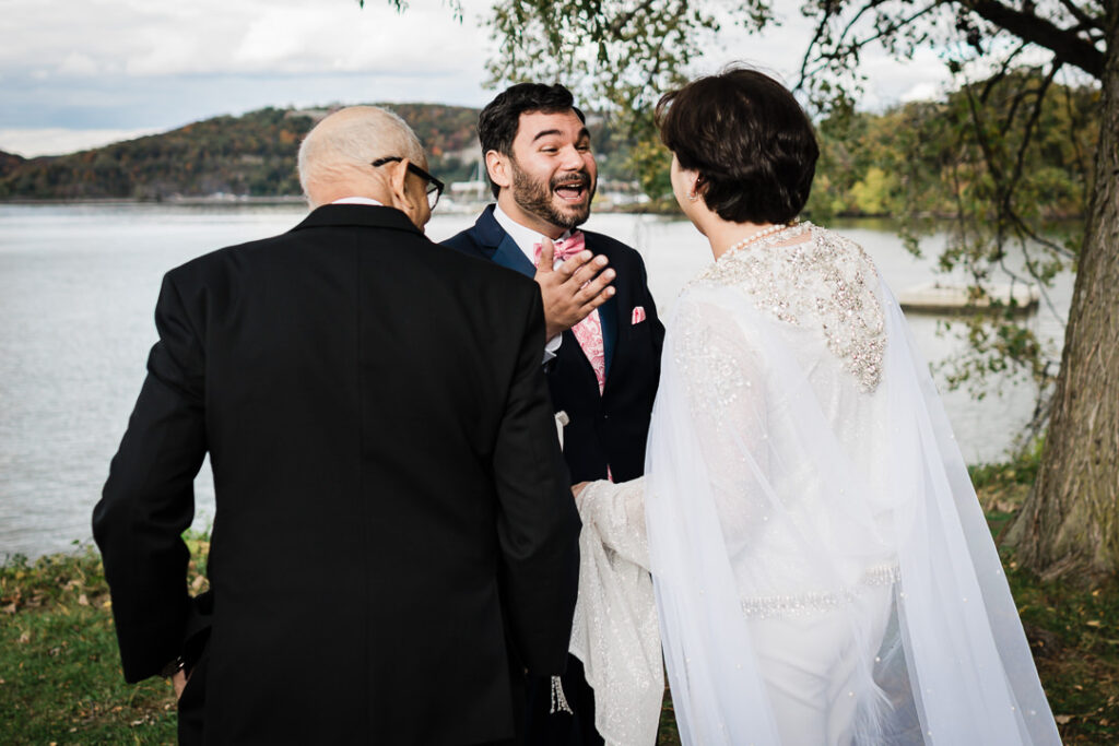 Couple sharing emotional first look with parents by Hudson River and fall mountains in Peekskill NY