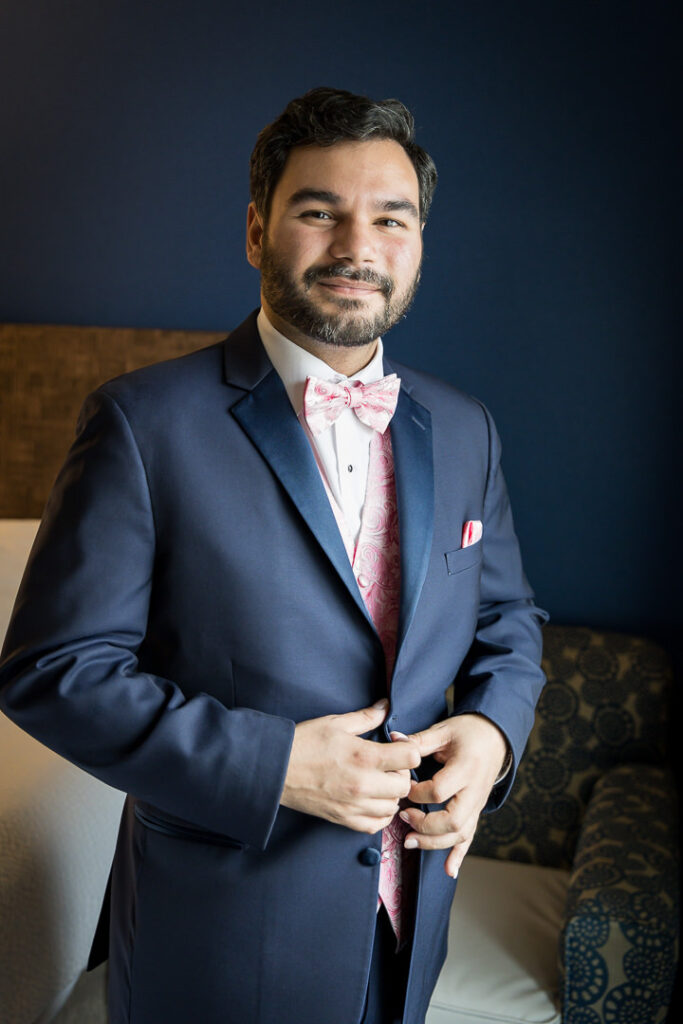 Groom in navy suit with pink paisley bow tie and boutonniere at Holiday Inn Express Peekskill wedding getting ready