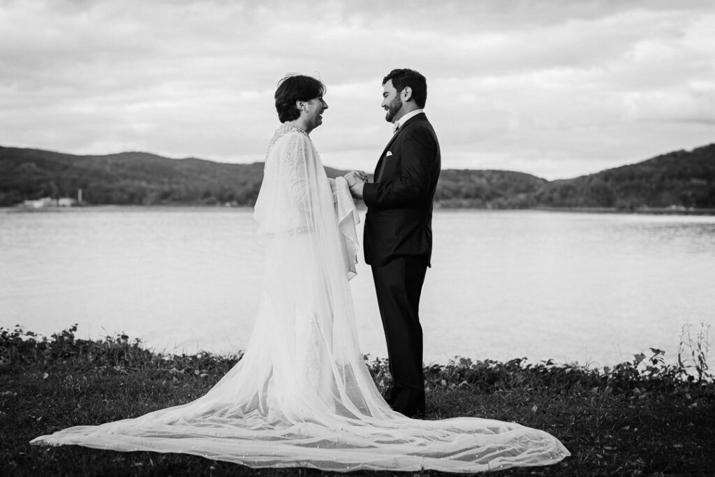 Black-and-white portrait of couple holding hands by Hudson River with veil, timeless wedding photo