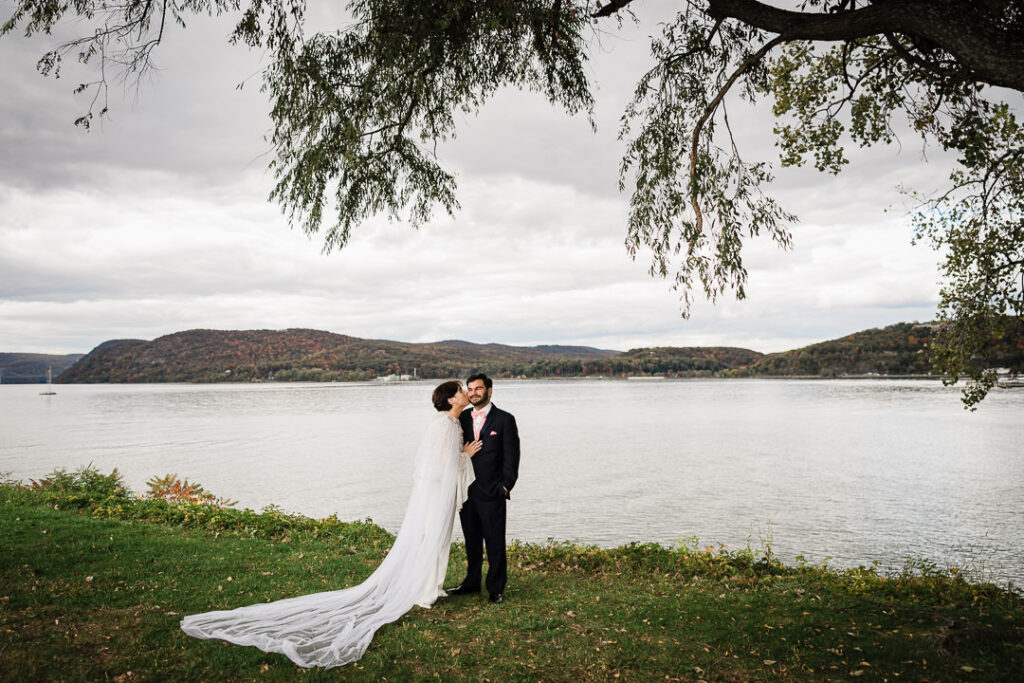 Couple sharing kiss under willow branches with Hudson River view, artistic wedding photography
