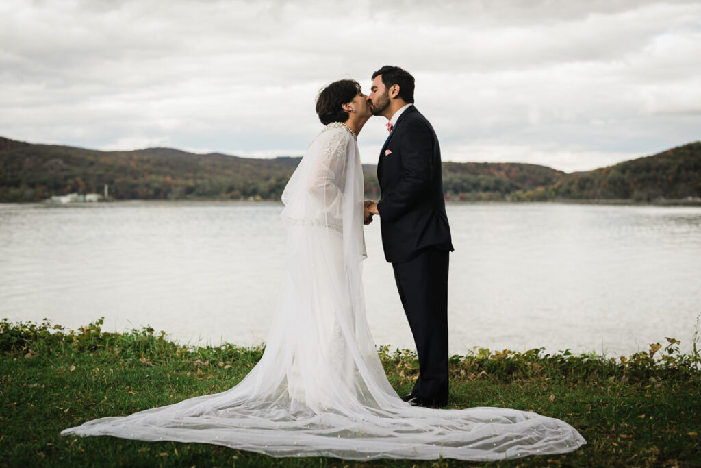 Couple kissing by Hudson River with flowing cathedral veil and fall mountains, Peekskill NY wedding