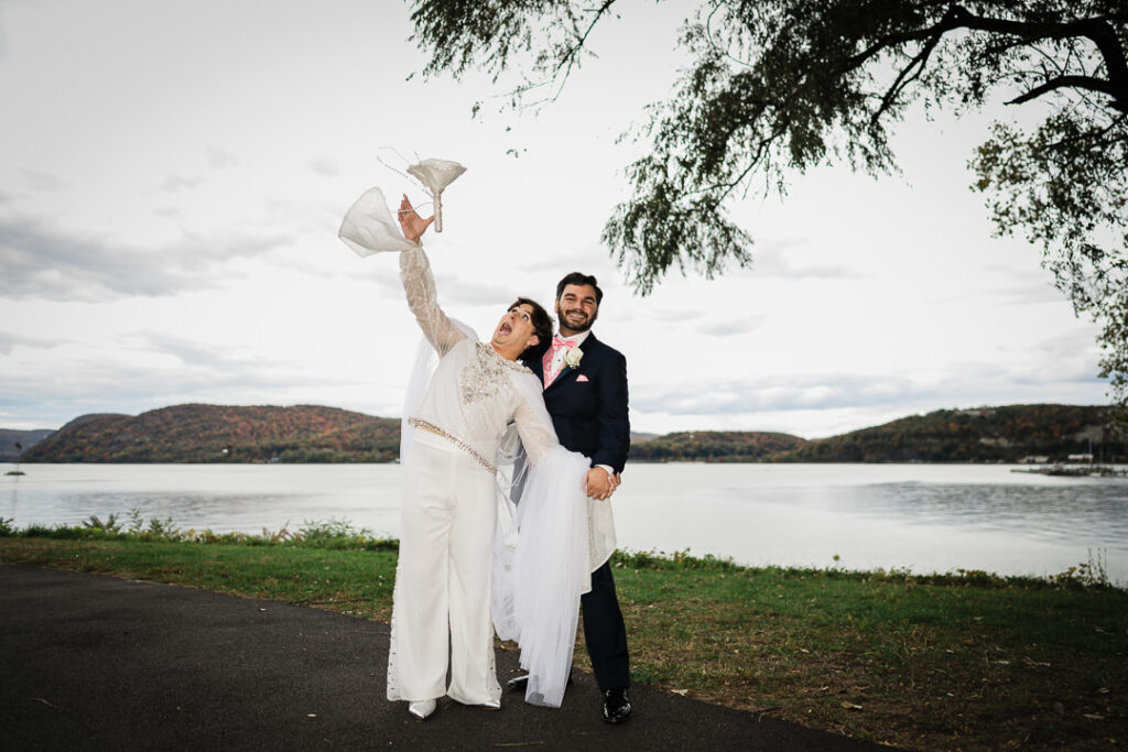 Playful moment of veil toss as couple laughs by Hudson River, Peekskill waterfront wedding