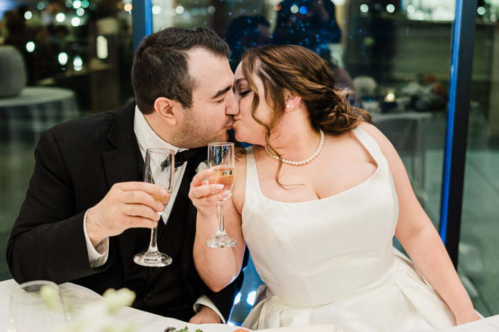 Newlyweds kissing while toasting with champagne glasses.