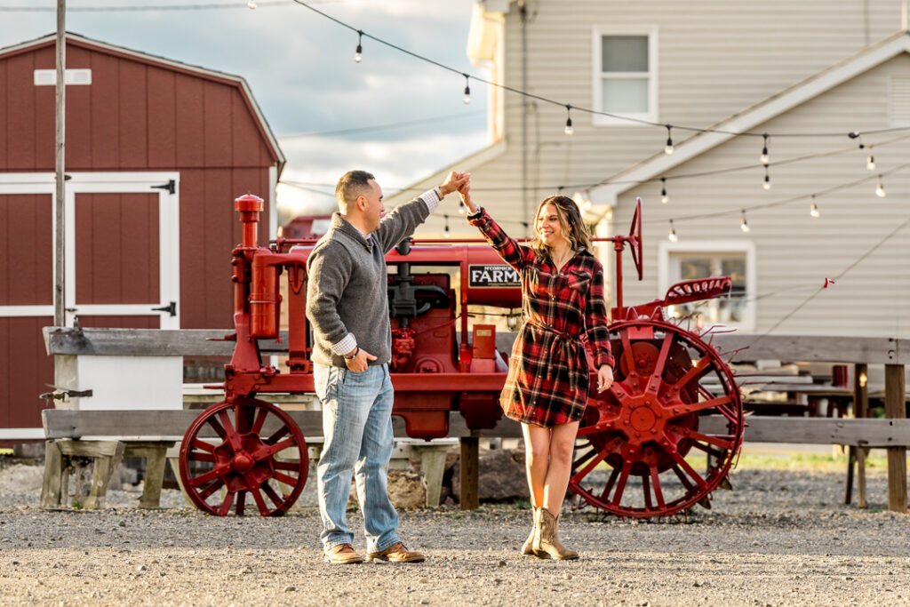 Engaged couple dancing beside a vintage red tractor during a rustic farm engagement session