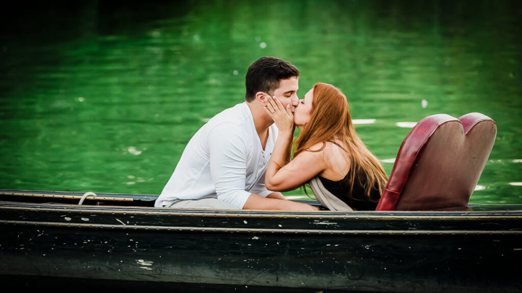 Couple sharing intimate kiss while sitting in vintage boat on emerald green water