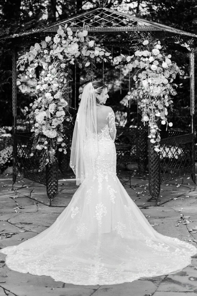 Back view of bride's lace wedding dress with long train at ceremony gazebo black and white