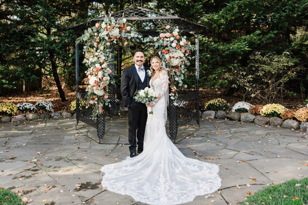 Bride and groom formal portrait under black gazebo with coral and eucalyptus floral arch at The English Manor
