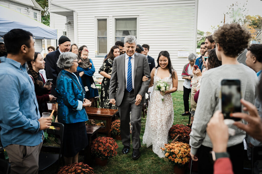 Bride processional down grass aisle lined with fall mums at outdoor ceremony in New Jersey