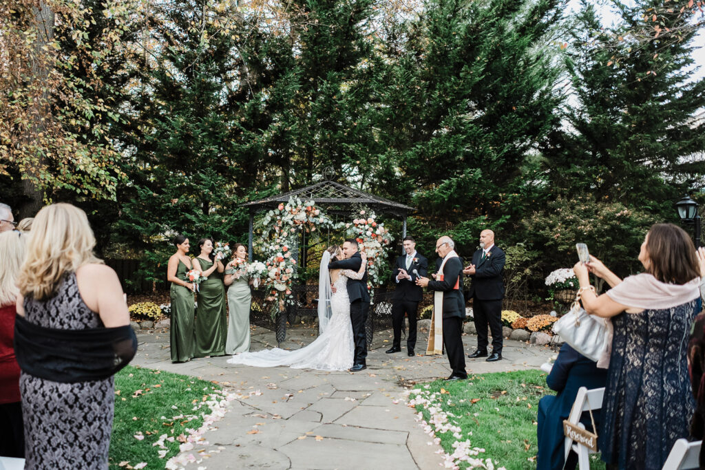 Wedding ceremony from guest perspective showing couple kissing at gazebo altar