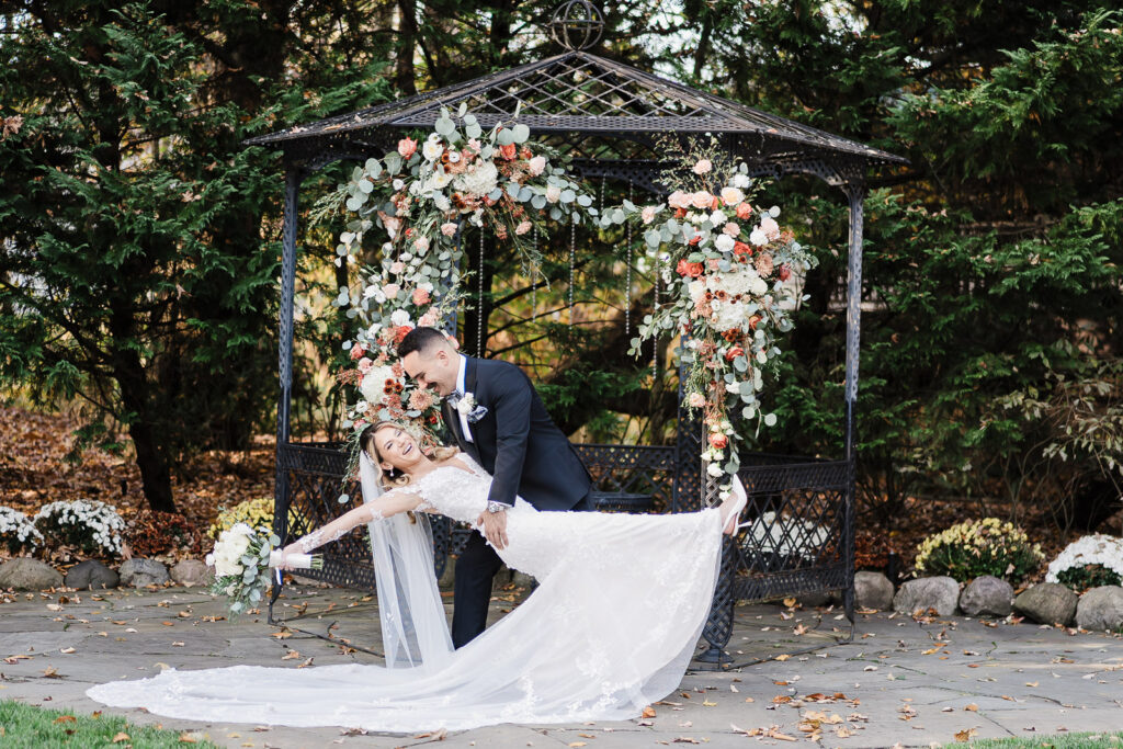 Groom dipping bride with flowing veil at ceremony gazebo after English Manor wedding