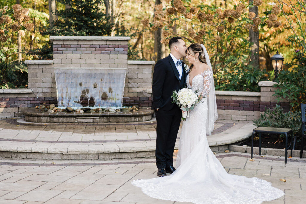 Wedding couple kissing at stone fountain with fall trees at The English Manor