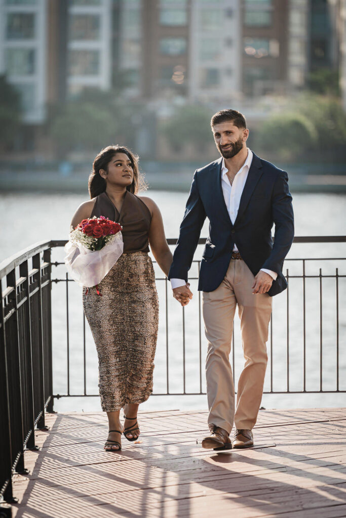 Couple walking on waterfront boardwalk at NYC engagement session by Alex Kaplan Photography