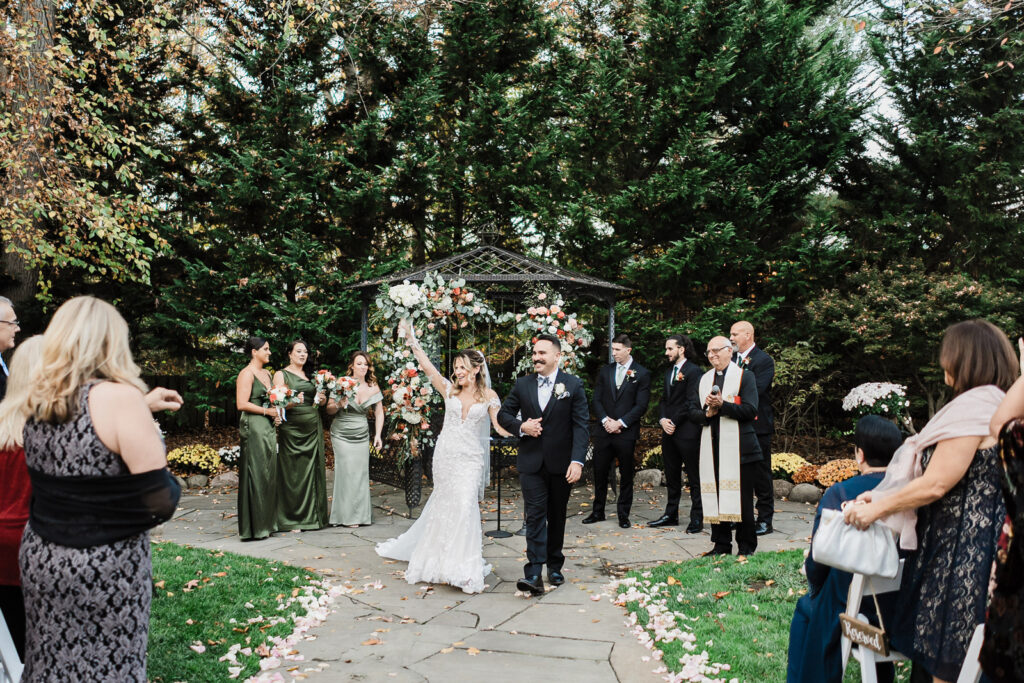 Bride celebrating with bouquet raised walking down aisle as newlyweds at The English Manor