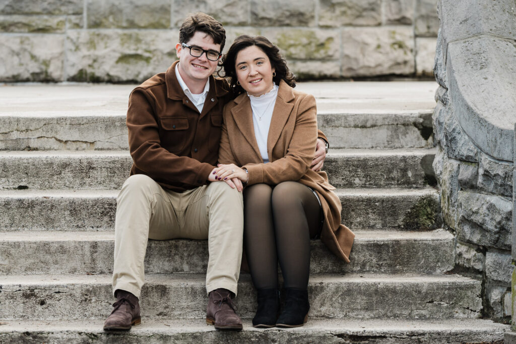 Shannon and Aidan sitting together on historic stone stairs during their Verona Park engagement session with Alex Kaplan Photography