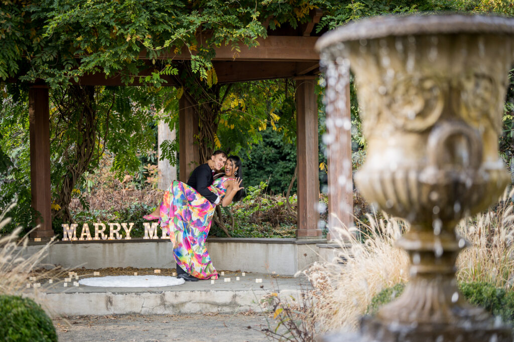Engaged couple walking through botanical garden surrounded by bright autumn foliage
