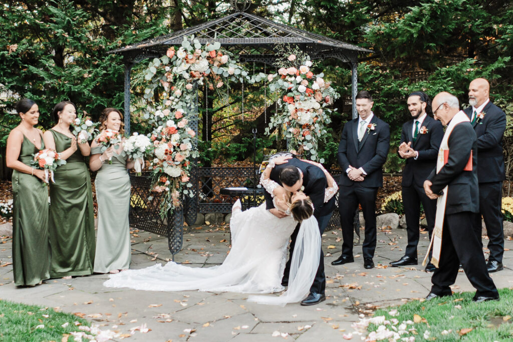 Couple sharing first kiss as married couple at gazebo ceremony with bridal party celebrating