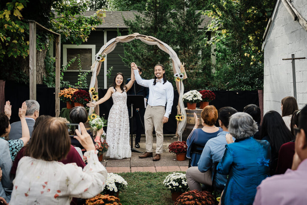 Couple celebrating after backyard wedding ceremony with raised arms in NJ