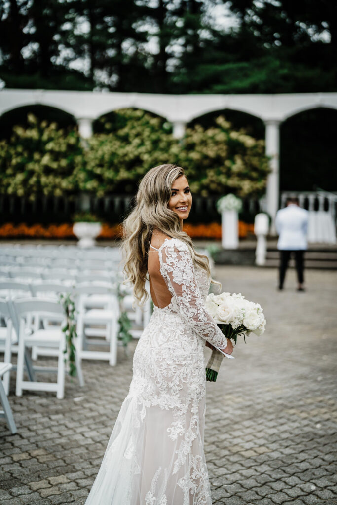 Bride showing gown back detail with bouquet at Legacy Castle colonnade by Alex Kaplan