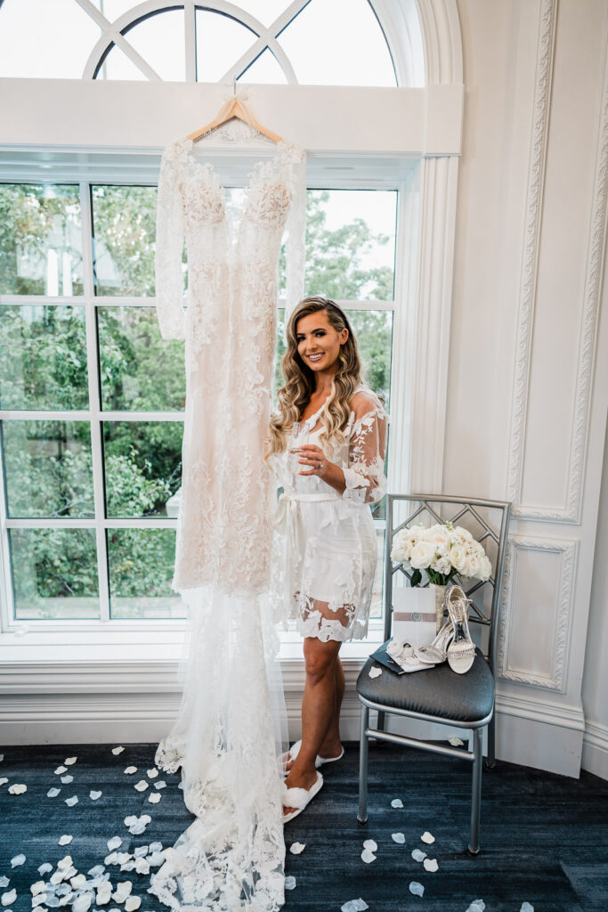 Bride in white floral robe with hanging wedding dress at Legacy Castle by Alex Kaplan Photography