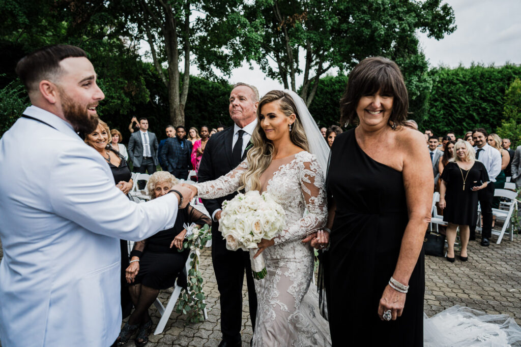 Bride reaching for groom's hand during ceremony at Legacy Castle Pompton Plains wedding by Alex Kaplan