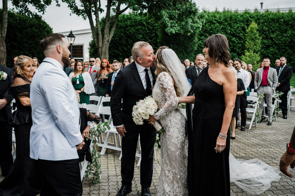 Father kissing bride during wedding ceremony processional at The Legacy Castle photographed by Alex Kaplan