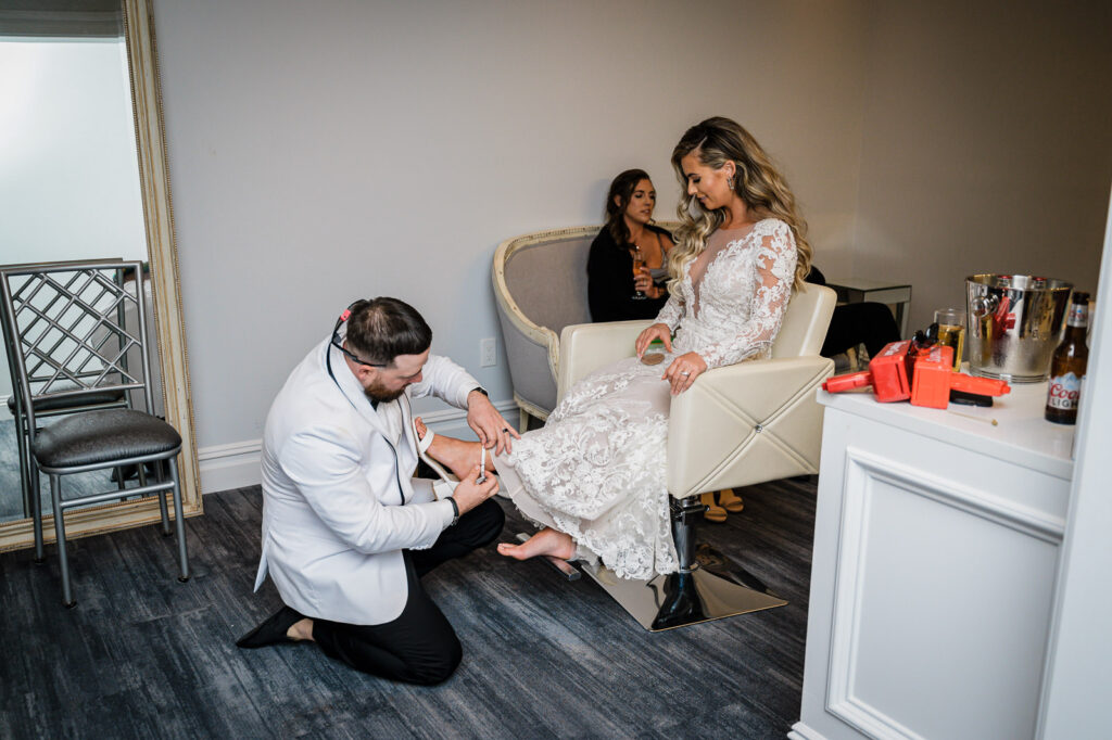 Groom writing on bride's shoe during getting ready at Legacy Castle wedding by Alex Kaplan Photography