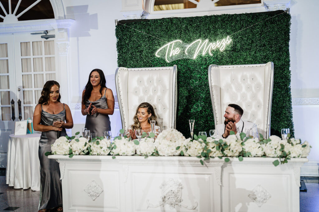 Couple at sweetheart table with custom hedge wall backdrop at Legacy Castle wedding by Alex Kaplan