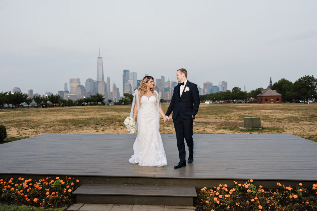 Bride and groom walking on boardwalk with cathedral veil and NYC Manhattan skyline at Liberty State Park by Alex Kaplan Photography
