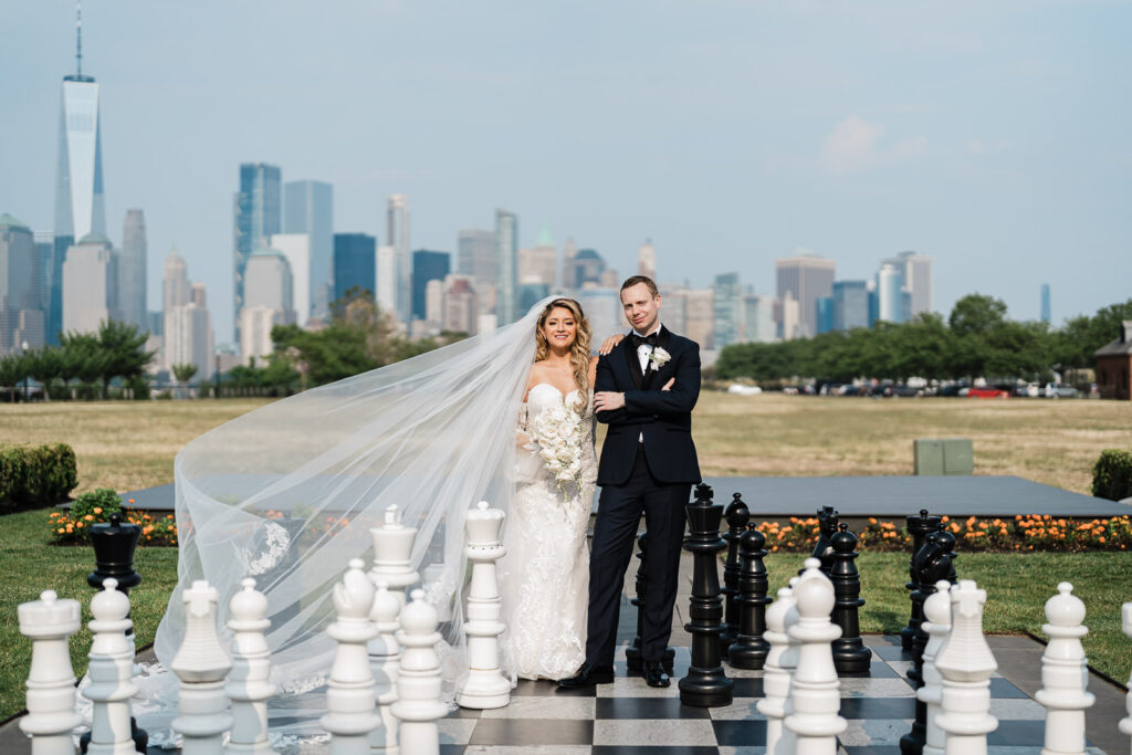 Bride and groom wedding portraits at giant outdoor chess set with NYC skyline at Liberty House Jersey City by Alex Kaplan Photography
