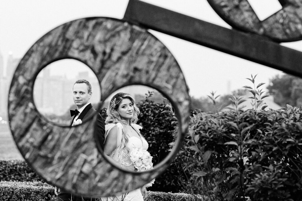 Creative wedding portrait of bride and groom framed through circular sculpture at Liberty State Park Jersey City by Alex Kaplan Photography