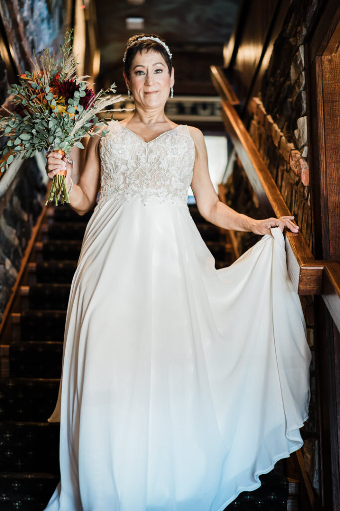 Bride in lace wedding gown with fall bouquet on wooden staircase at Mohawk House Sparta NJ by Alex Kaplan Photography