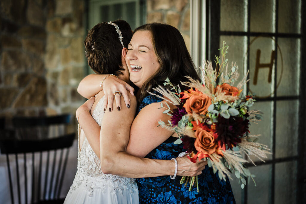 Bride shares emotional hug with wedding guest while holding fall bouquet at Mohawk House in Sparta NJ by Alex Kaplan
