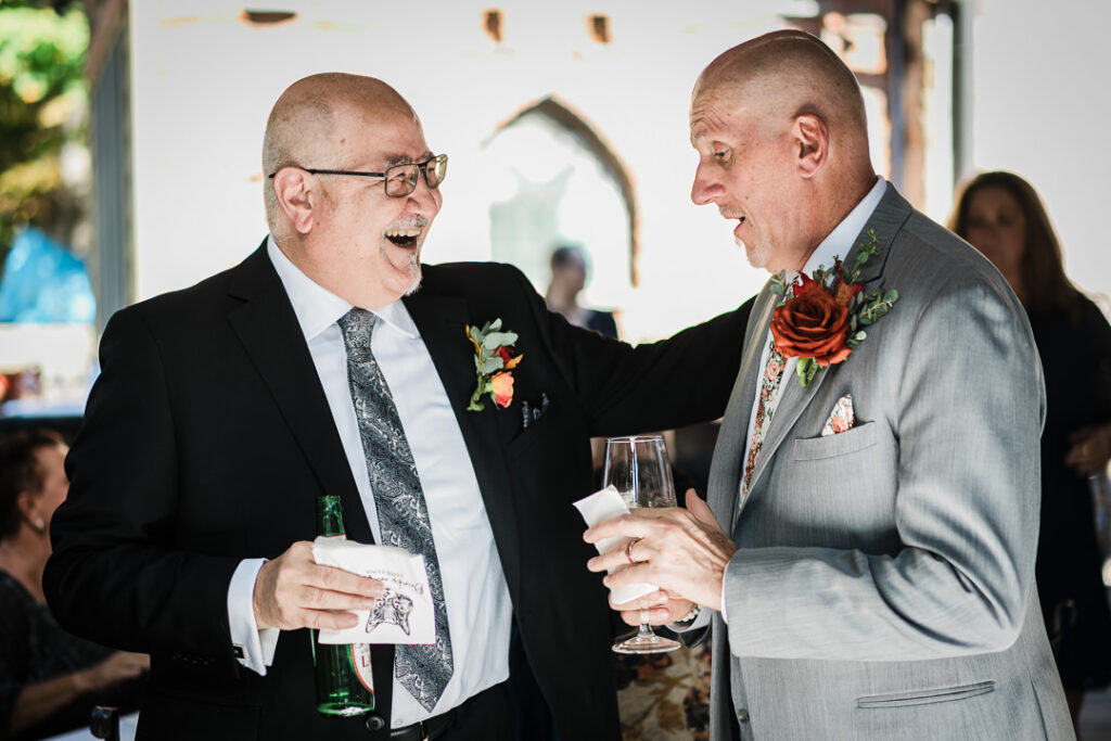 Groom laughs with wedding guest during outdoor cocktail hour at Mohawk House Sparta NJ by Alex Kaplan
