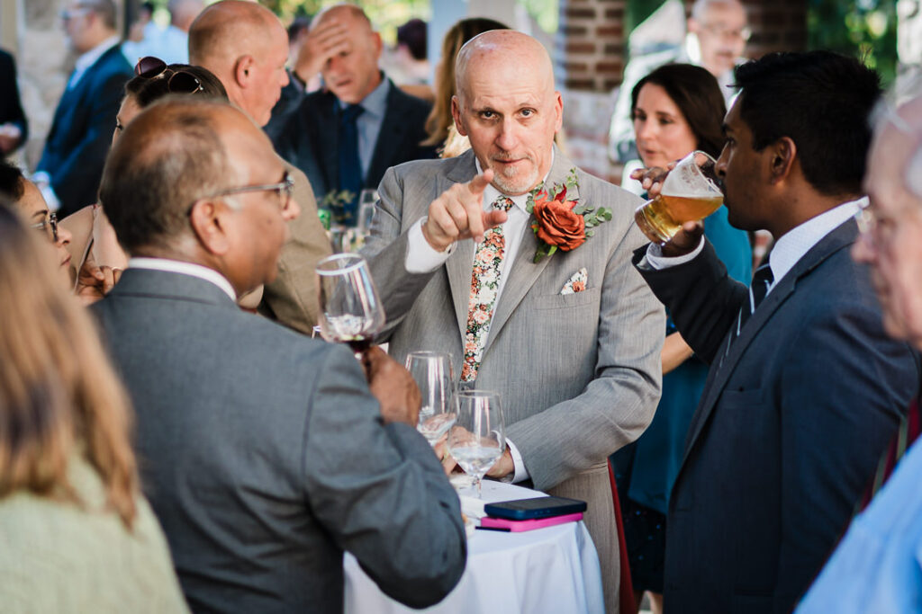 Candid moment of groom conversing with guests at Mohawk House cocktail hour Sparta NJ by Alex Kaplan