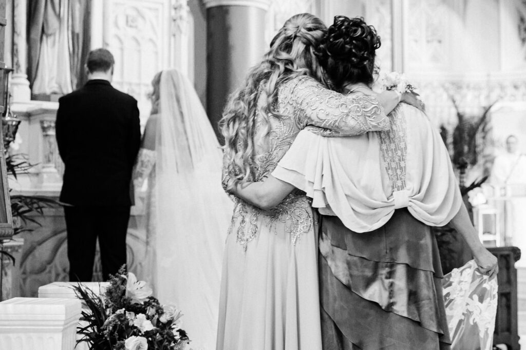 Mothers embracing during emotional candle ceremony at St. Henry's Church Catholic wedding by Alex Kaplan Photography