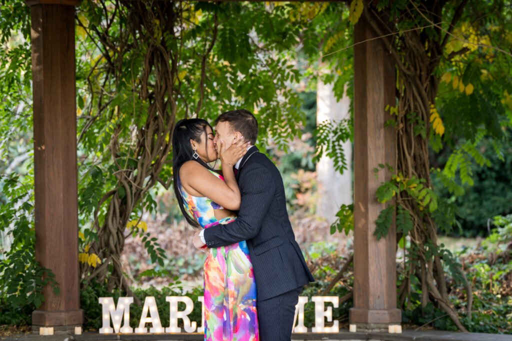 Newly engaged couple celebrating under pergola with MARRY ME letters during fall afternoon