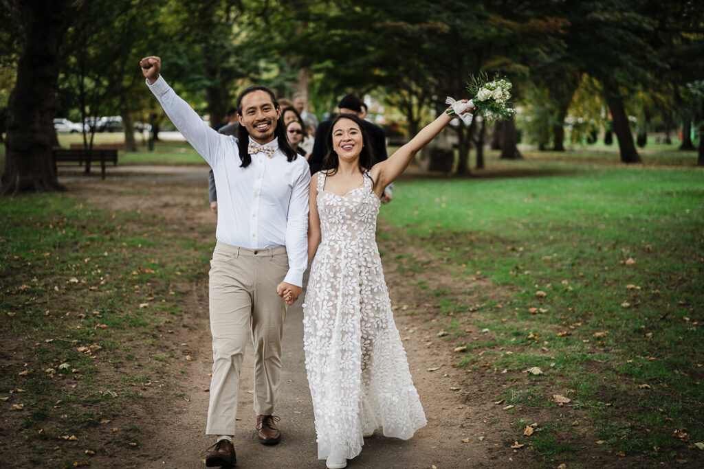 Joyful couple celebrating marriage in park with raised arms in NJ
