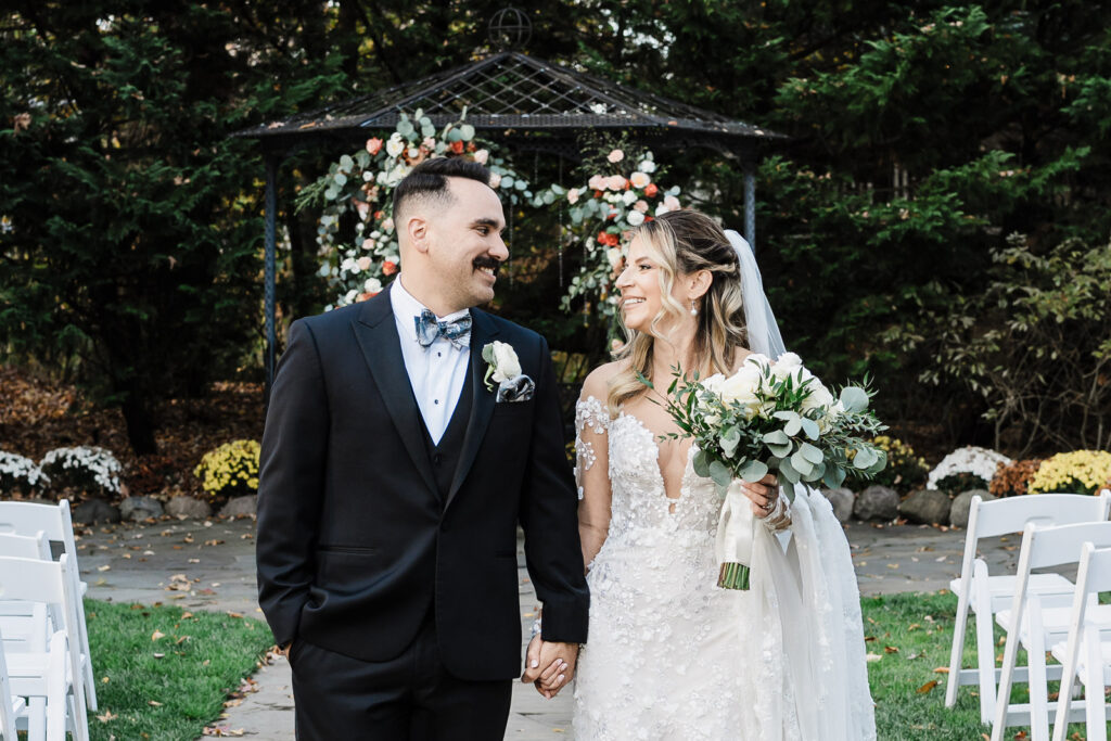 Newlyweds holding hands and smiling after ceremony at The English Manor gazebo