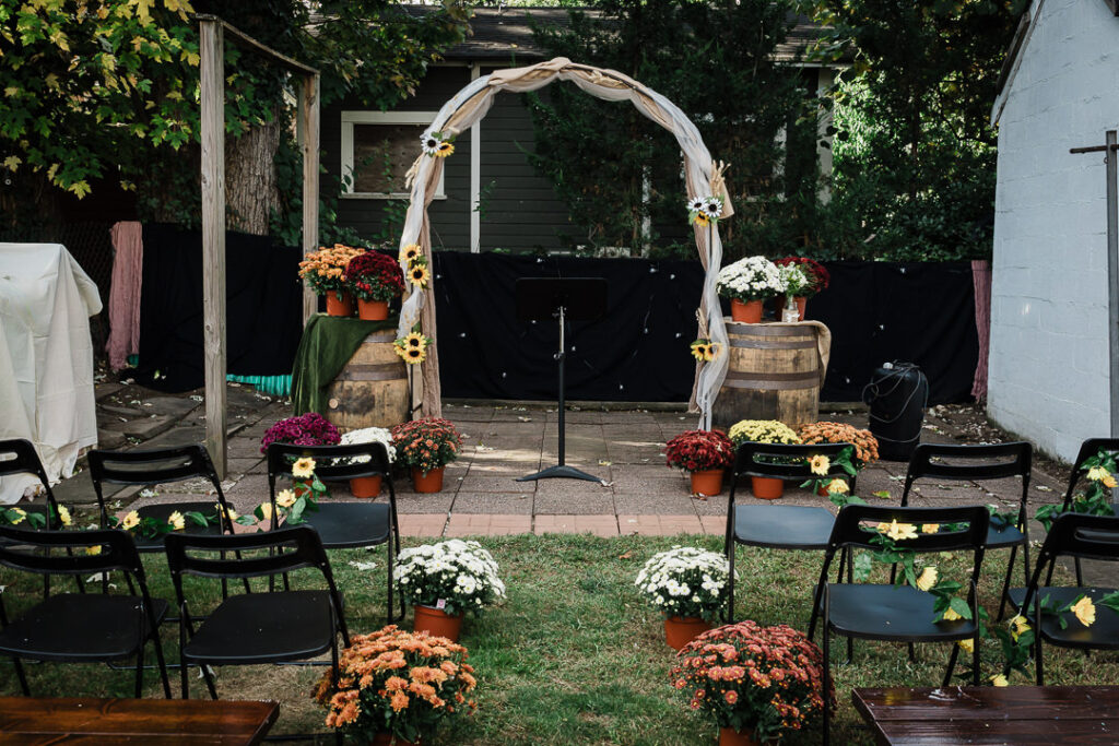 Rustic outdoor wedding ceremony with burlap arch, sunflowers, and colorful autumn mums in NJ