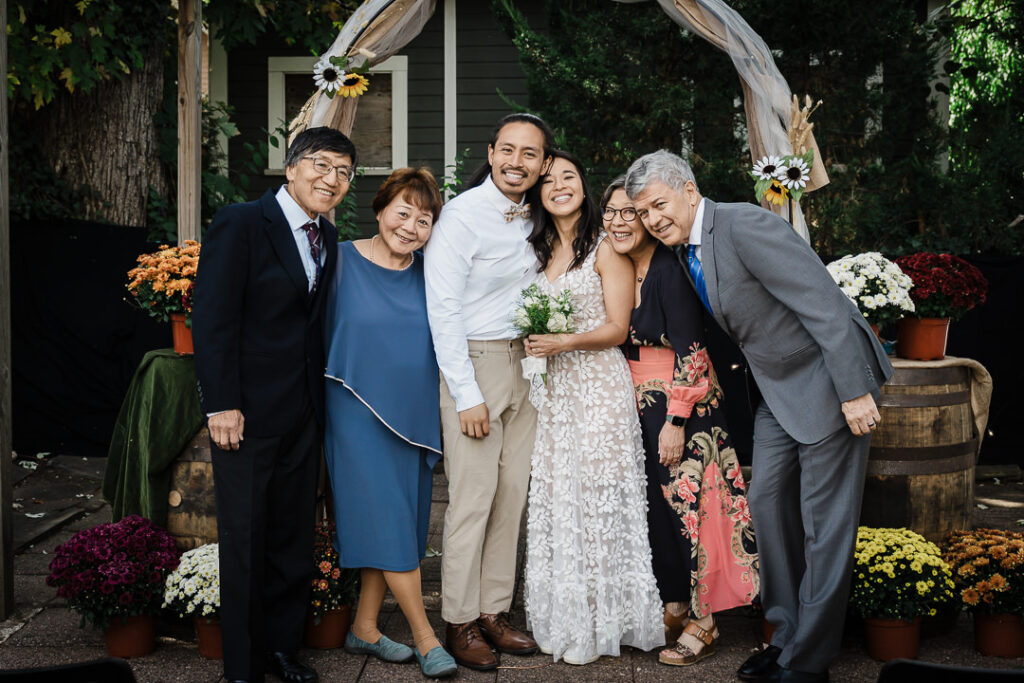 Happy couple with parents in front of rustic wedding arch with fall flowers at NJ wedding
