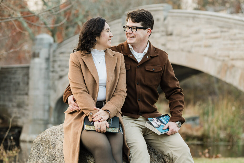 Shannon and Aidan sitting on rock with books during engagement session at Verona Park photographed by Alex Kaplan