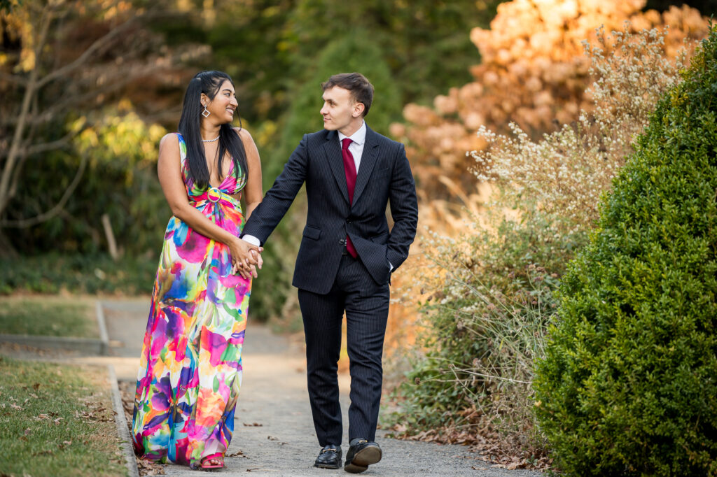 Playful engaged couple laughing beside pergola during fall botanical garden engagement