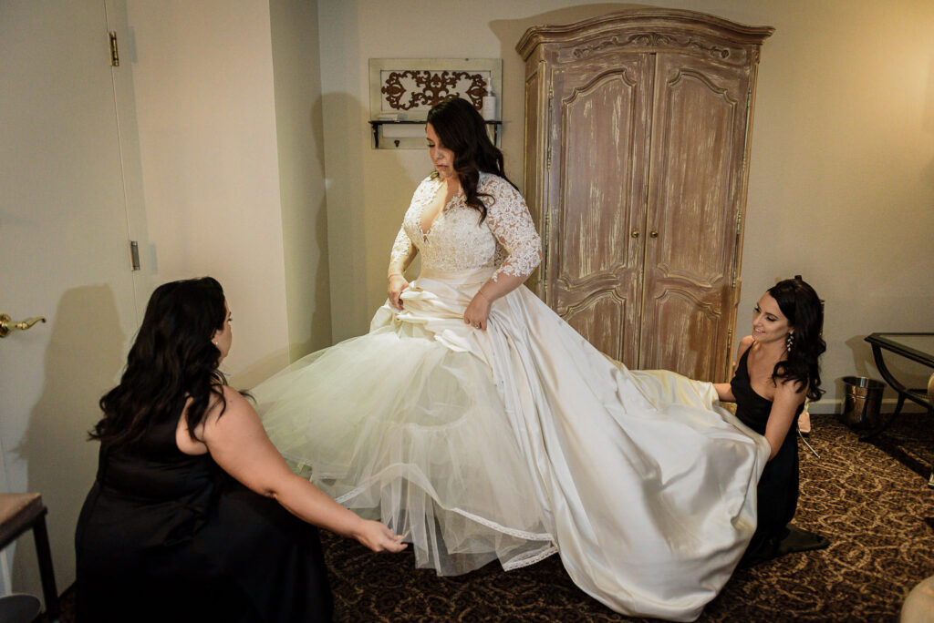 Bride in lace ball gown being helped by bridesmaids at Ramsey Country Club wedding by Alex Kaplan