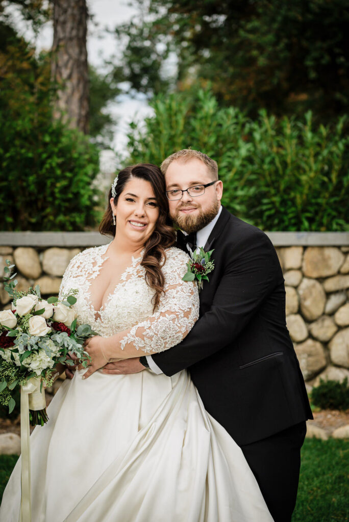 Happy couple embracing by stone wall at Ramsey Country Club fall wedding Alex Kaplan Photography
