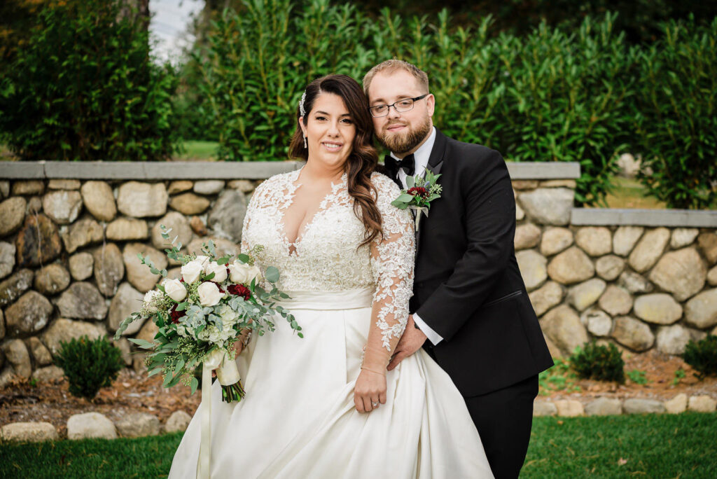 Bride and groom by fieldstone wall with greenery at Ramsey Country Club by Alex Kaplan