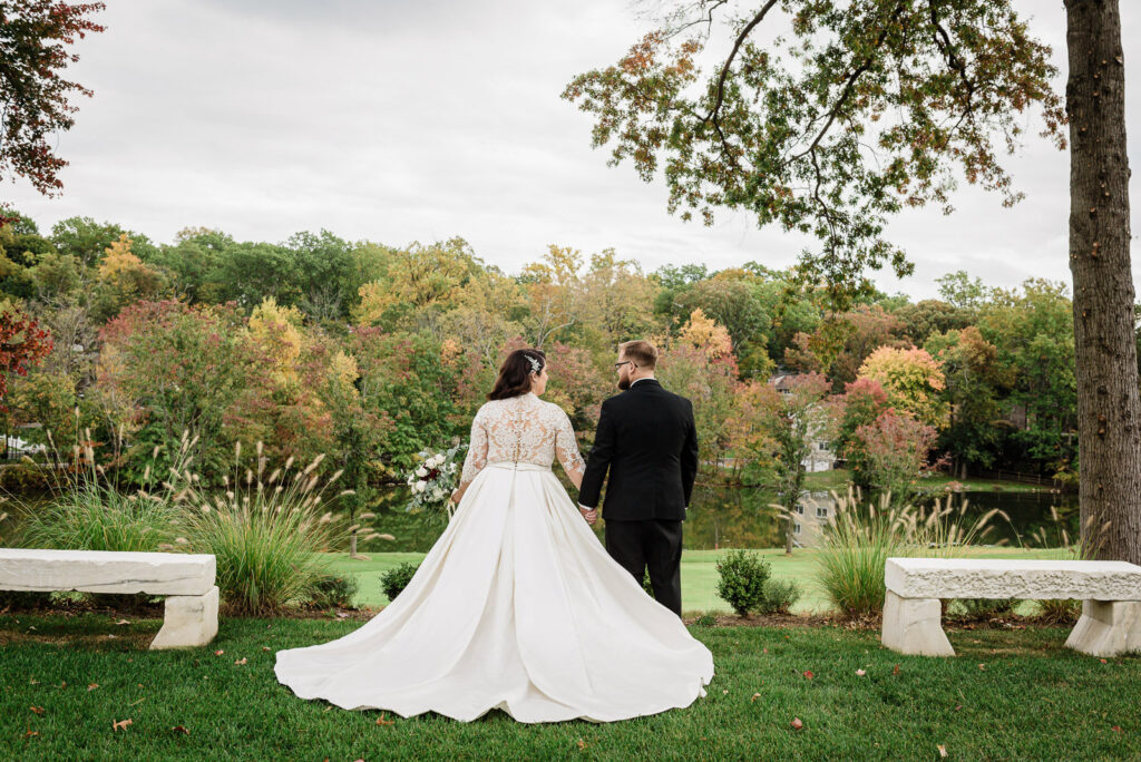 Bride and groom walking hand in hand with lake and fall colors at Ramsey Country Club by Alex Kaplan Photography