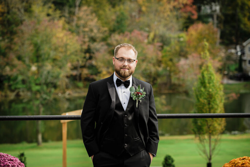 Groom in black tuxedo with burgundy boutonniere at Ramsey Country Club fall wedding by Alex Kaplan