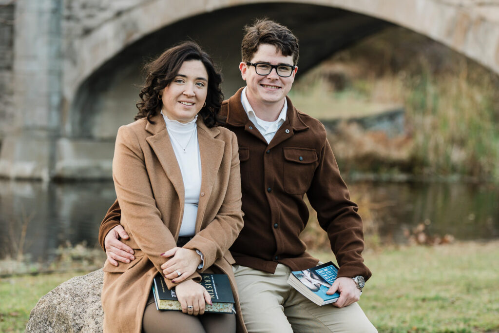 Engaged couple sitting with books near historic stone bridge at Verona Park by Alex Kaplan Photography